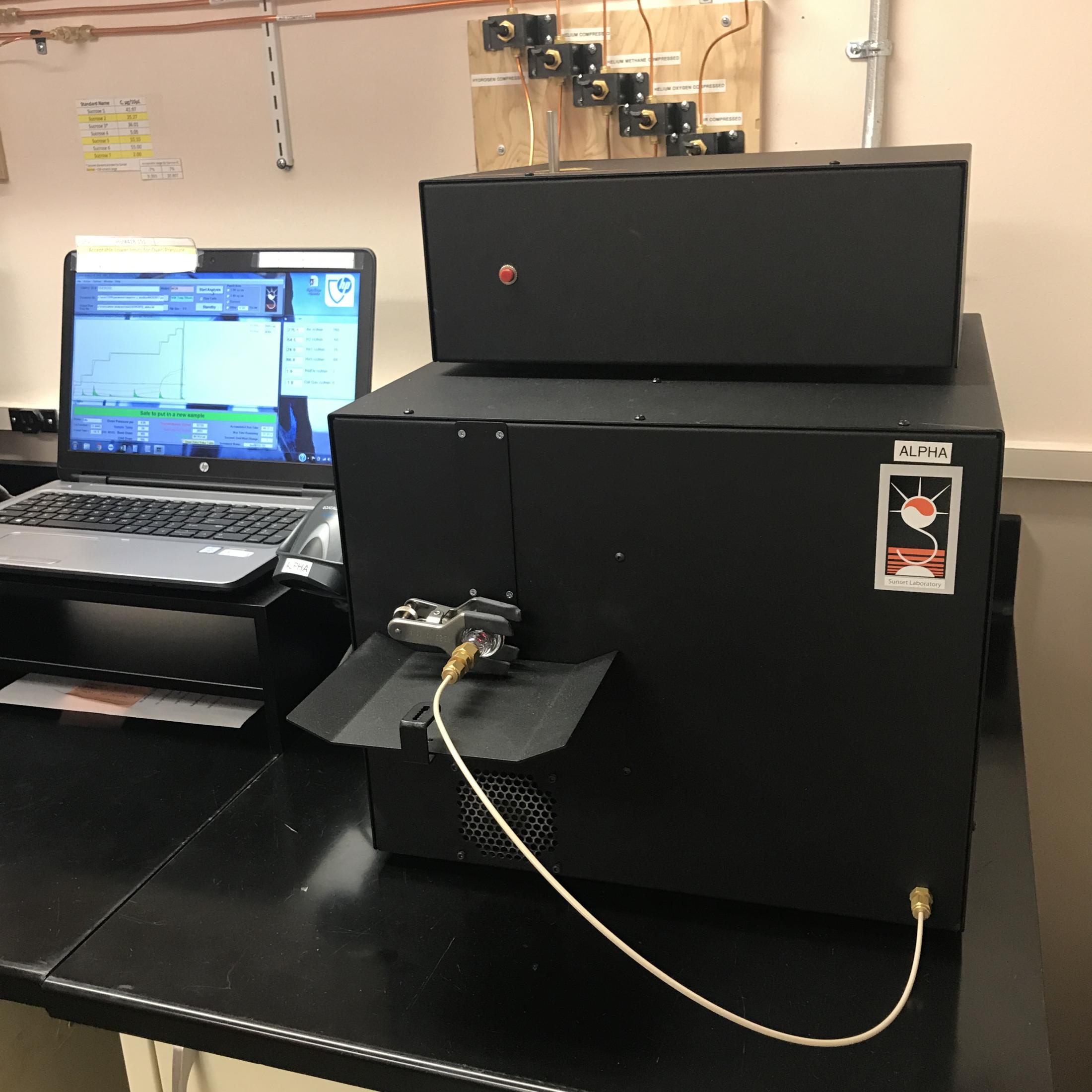 Image: a black box instrument next to a laptop displaying graph readouts.