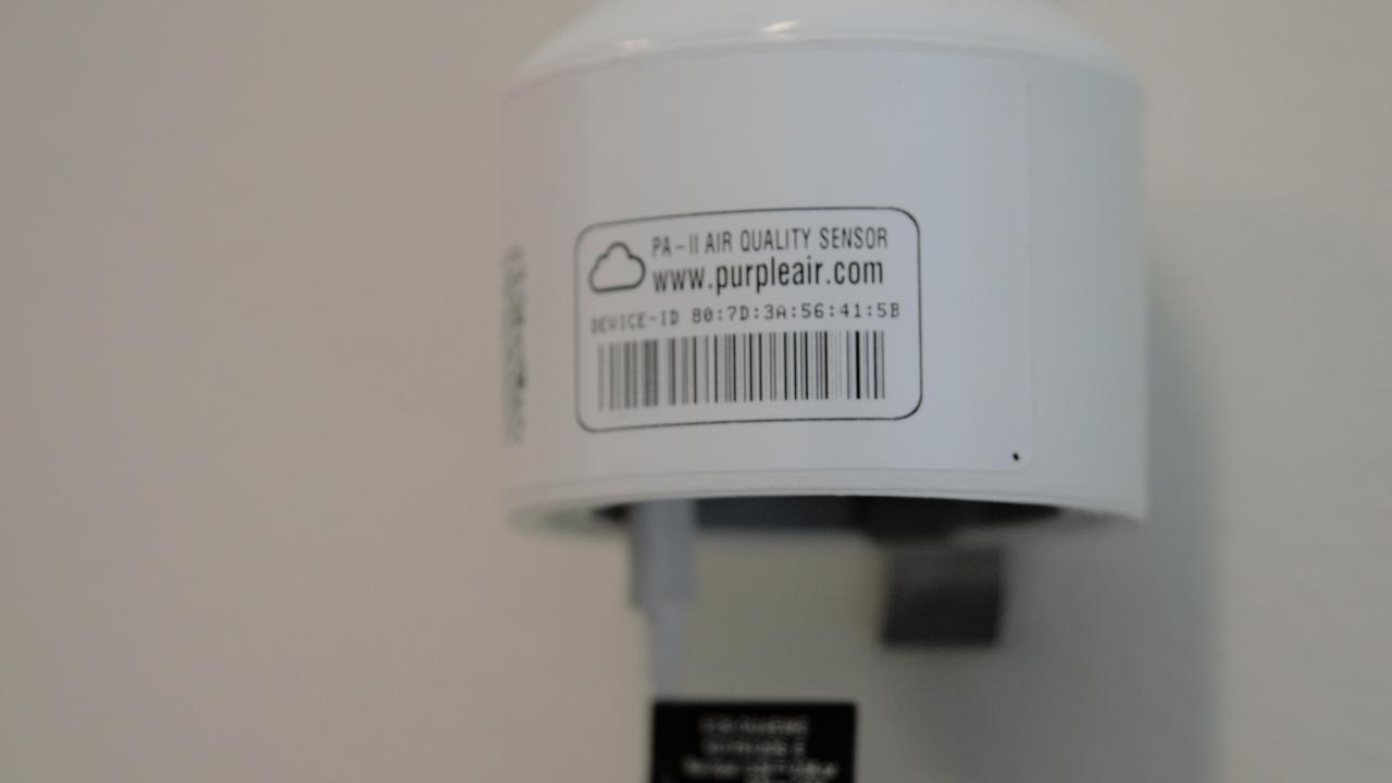 Image: a white PVC cap PurpleAir sensor, mounted on a wall.