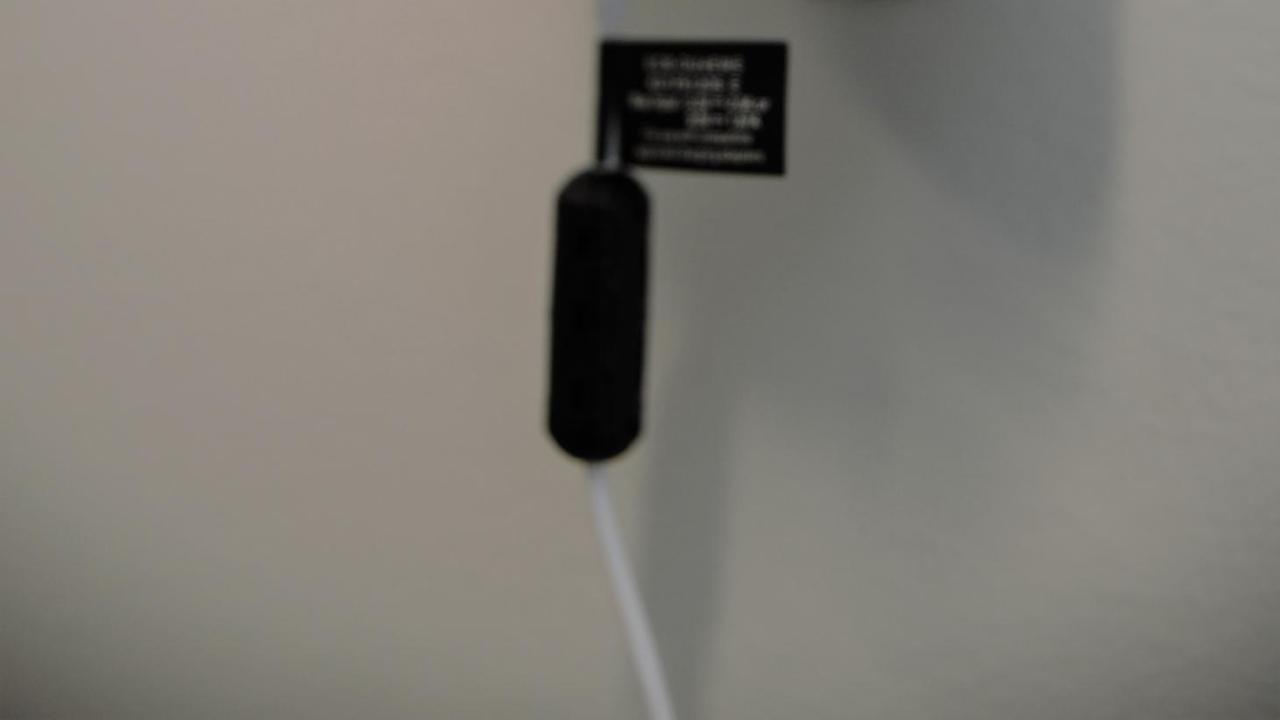 Image: a white PVC cap PurpleAir sensor, mounted on a wall.