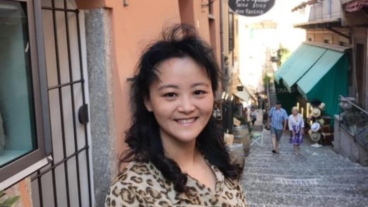 Image: photo of Qi Zhang, who stands in front of an outdoor shop.