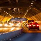 Image: a vehicular tunnel with cars driving through.