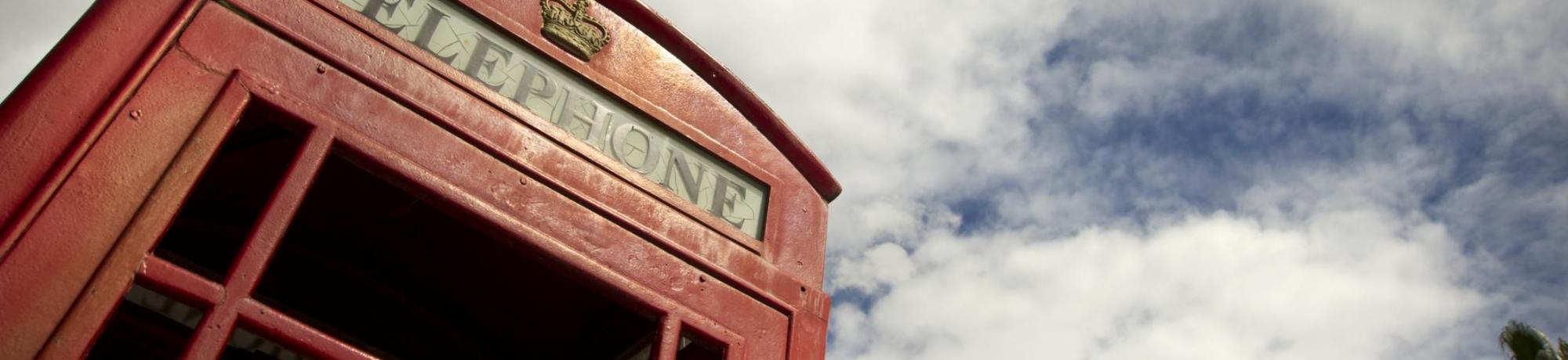 Image: vintage red phone booth and cloudy blue sky overhead.